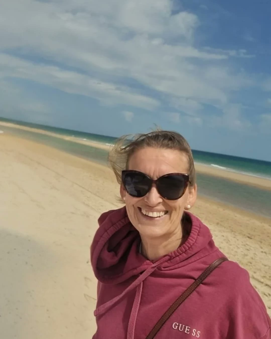 Sara smiling on a windswept beach in the Algarve, sea and lagoon behind her
