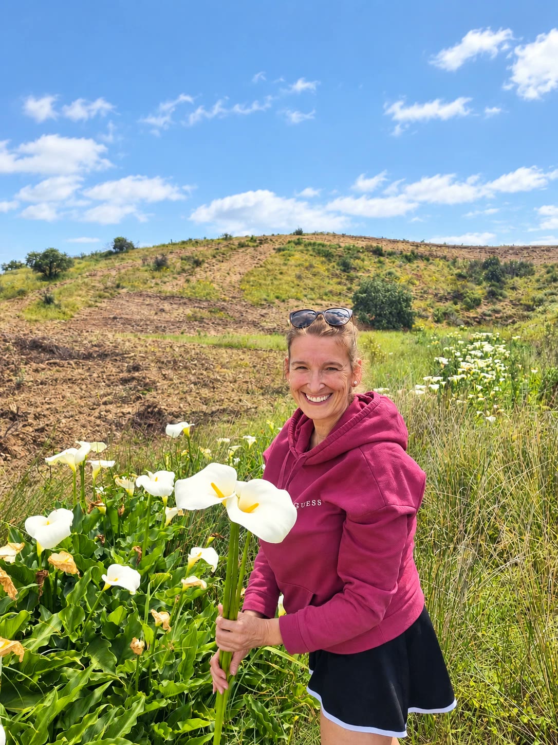 Sara smiling on her land in the East Algarve, holding wild calla lilies